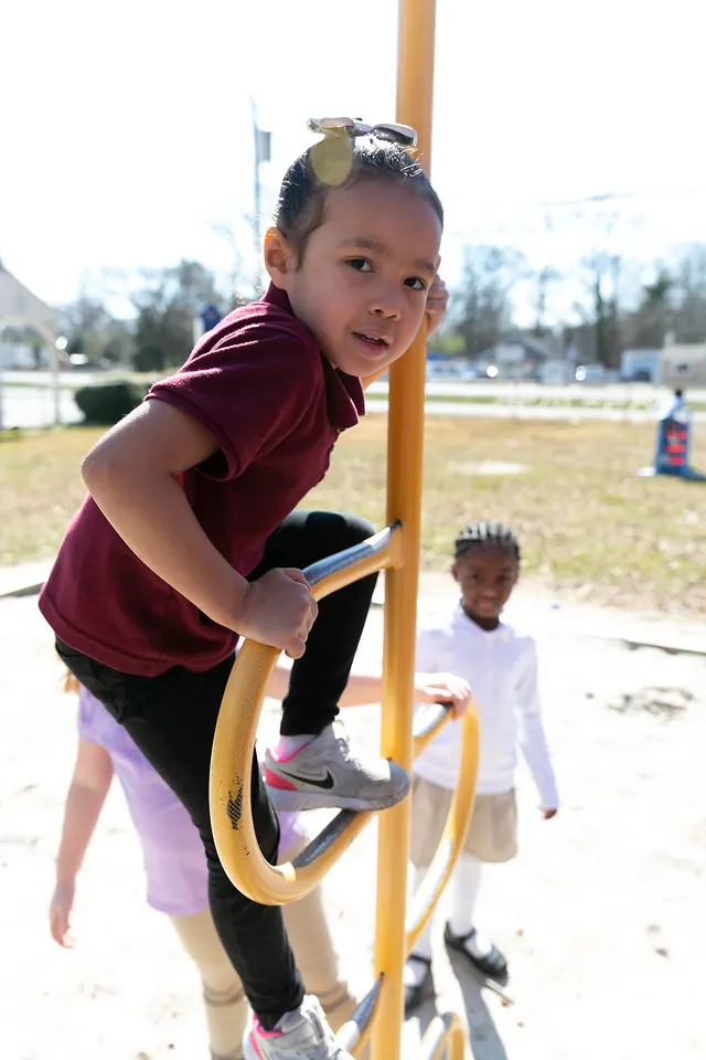A girl climbing playground equipment with a big smile