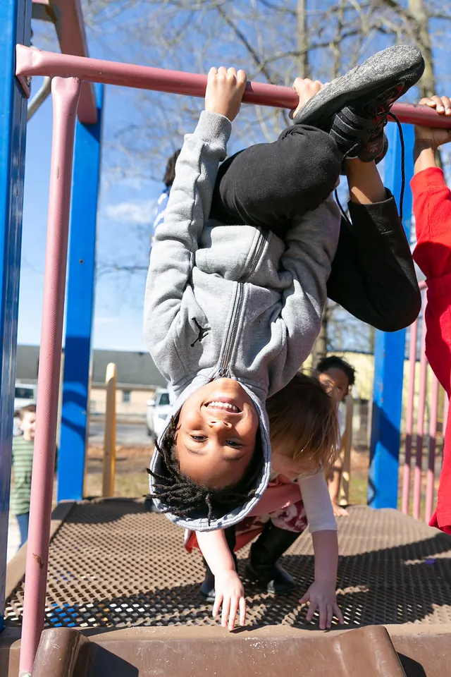 A child hanging upside down on the monkey bars