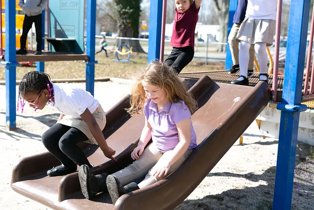 Two girls sliding down the playground slide