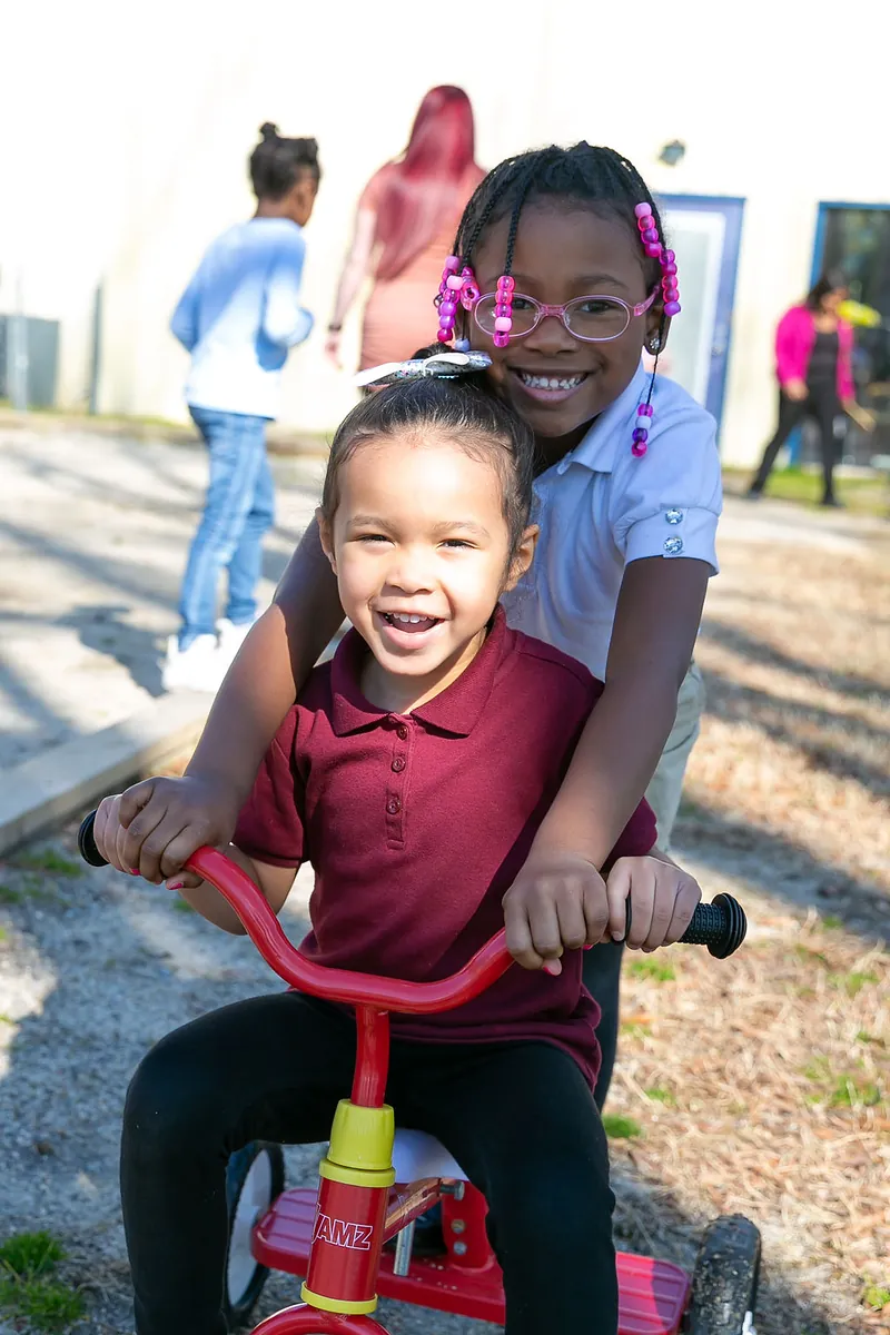 Two girls riding a tricycle together outdoors